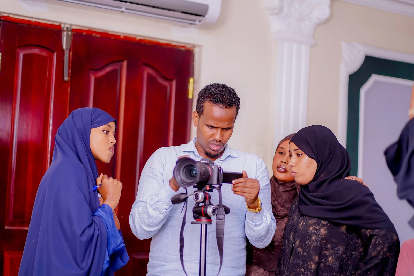 A trainer demonstrating a tripod-mounted camera to participants of the audiovisual production training.
