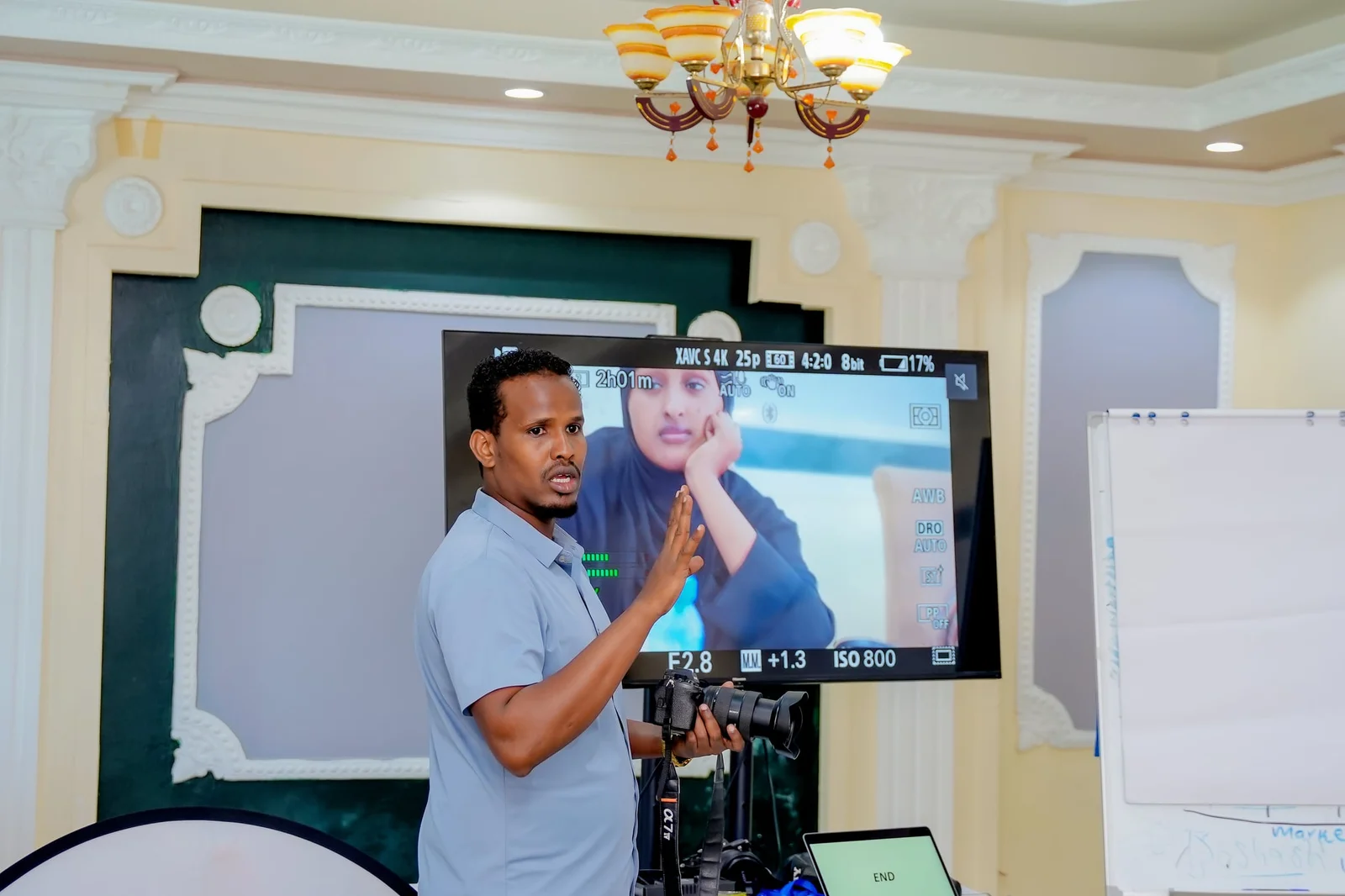 A trainer explaining camera settings shown on a live monitor during the audiovisual production training.